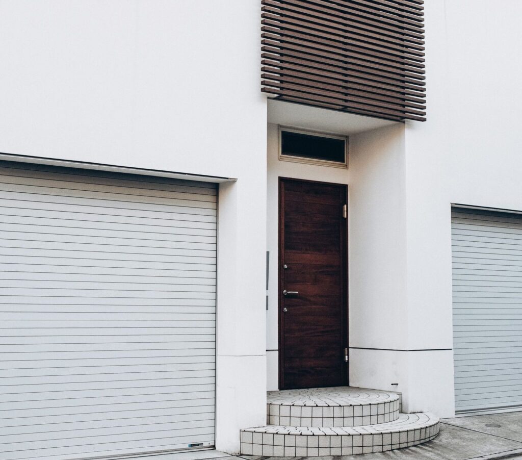 Contemporary white building facade with wooden door and twin garage entrances.